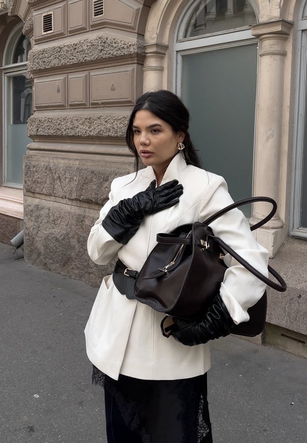 Witte getailleerde blazer, zwarte leren handschoenen, zwarte handtas met metalen details. Getextureerd oppervlak, formeel ontwerp, contrasterende kleuren.