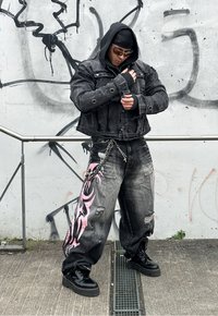 Μαύρο τζάκετ από τζιν με κοντή σχεδίαση και ασημένιες λεπτομέρειες, σε συνδυασμό με κατεστραμμένα μαύρα τζιν με ροζ φυλετικά μοτίβα. Ογκωτά μαύρα μποτίνια.