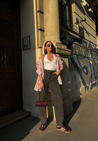 Camisa de rayas rosa claro de gran tamaño, top blanco de tirantes, pantalones cargo oscuros, bolso cruzado burdeos y zapatillas burdeos con rayas blancas.
