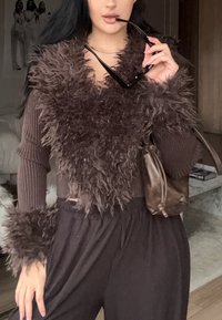 Pulover maro scurt cu guler și manșete din blană pufoasă, asortat cu pantaloni înalți pe talie de culoare închisă și o geantă maro. Textură netedă a țesăturii.