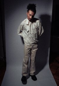 T-shirt crème surdimensionnée avec un motif floral texturé, associée à un pantalon beige clair. Tissu lisse et coupe décontractée, complétée par des chaussures noires.