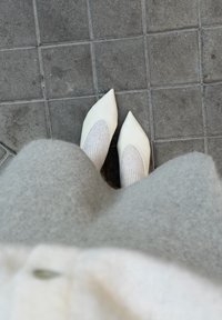 Valged teravnurkse otsaga kingad lõikega detailiga, kombineeritud heledate hallide sooniklike sokkidega. Pehme hall kangas langeb alumise serva kohale. Tekstuuriga kõnnitee all.