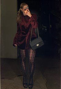 Bordeaux fluwelen blazer, doorschijnend zwart kanten topje, zwarte panty met kanten patroon, zwarte open-teen hakken en een zwarte gewatteerde handtas met gouden accenten.