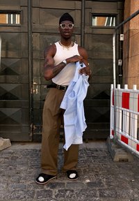 Šviesiai mėlyna marškinėliai, laikomi asmens, apsirengusio baltu rankovėmis marškinėlių, rudos spalvos plačiomis kelnėmis ir juodais sandalais su baltais akcentais, prieš tamsių medinių fono.