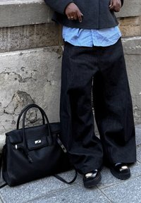 Fekete bőr kézitáska texturált felülettel, széles sötét farmernadrág, alatta kék-fehér csíkos ing, masszív fekete talpú cipők.