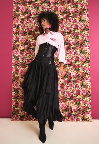 Saia preta em camadas com babados, corpete ajustado e camisa às riscas rosa. Inclui fundo floral com rosas e brincos ousados a condizer.