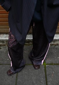 Pantalons à larges jambes en imprimé léopard avec des bandes roses sur les côtés, associés à des chaussures à motifs marron foncé, sous un blazer oversized à rayures.