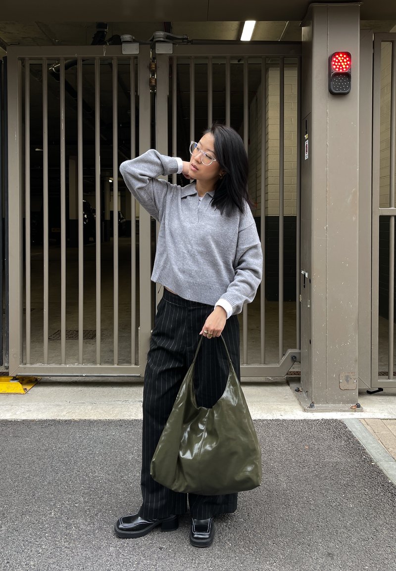 Pull gris court, pantalon noir à fines rayures, et un sac hobo vert olive brillant. Des lunettes claires et des chaussures à plateforme noires complètent le look.