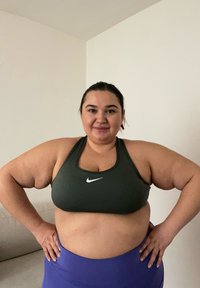 Zelená sportovní podprsenka s bílým logem Nike, v kombinaci s fialovými kalhotami s vysokým pasem. Hladká tkanina a p�řiléhavý design zdůrazňují sportovní oděv.