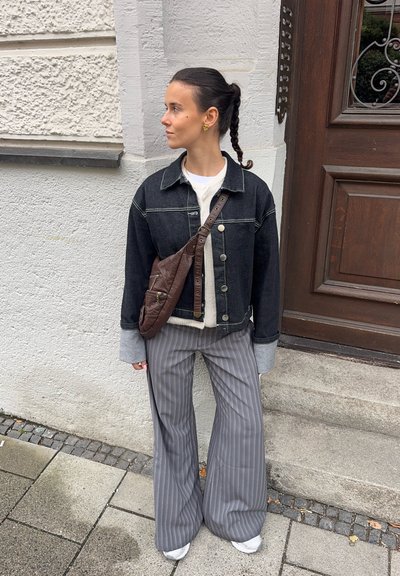 Chaqueta de mezclilla negra con botones plateados, pantalones de pierna ancha a rayas grises, suéter blanco y bolsa de bandolera marrón. Estilo sencillo, ajuste casual.