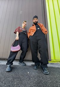 Μαύρες σαλοπέτες φορεμένες πάνω από ένα καφέ γραφικό μπλουζάκι, συνδυασμένες με ένα εμπριμέ πορτοκαλί μπουφάν. Τα αξεσουάρ περιλαμβάνουν μια μωβ τσάντα και μαύρα παπούτσια με πλατφόρμα.