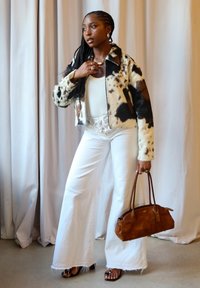 Faux fur jacket with black and brown spots, white fitted top, white flared trousers, brown suede handbag, and strappy black sandals.