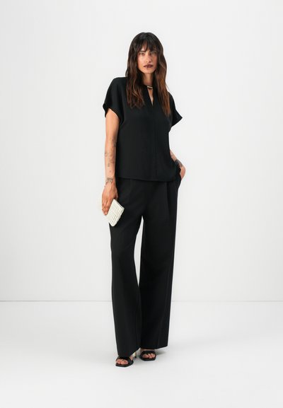 Top corto negro de manga corta con escote en V y corte holgado, combinado con pantalones negros de pierna ancha. Accesorios con un bolso de mano blanco texturizado.