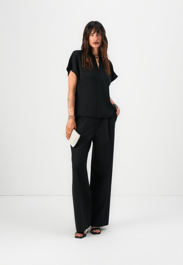 Cămașă neagră cu mâneci scurte și decolteu în V, într-o croială lejeră, asociată cu pantaloni negri cu picioare largi. Accesorizată cu o geantă albă texturată.