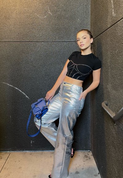 Top corto negro con pantalones metálicos plateados de cintura alta y un bolso bandolera azul. Los pantalones tienen una textura brillante y un ajuste estructurado.