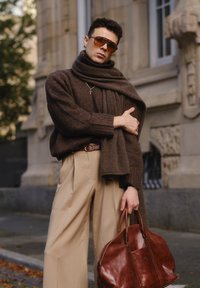 Ruske knitting pullover med en mørkebrun scarf, beige vidde bukser og en maroon lædertaske. Store brune solbriller; minimal smykker.