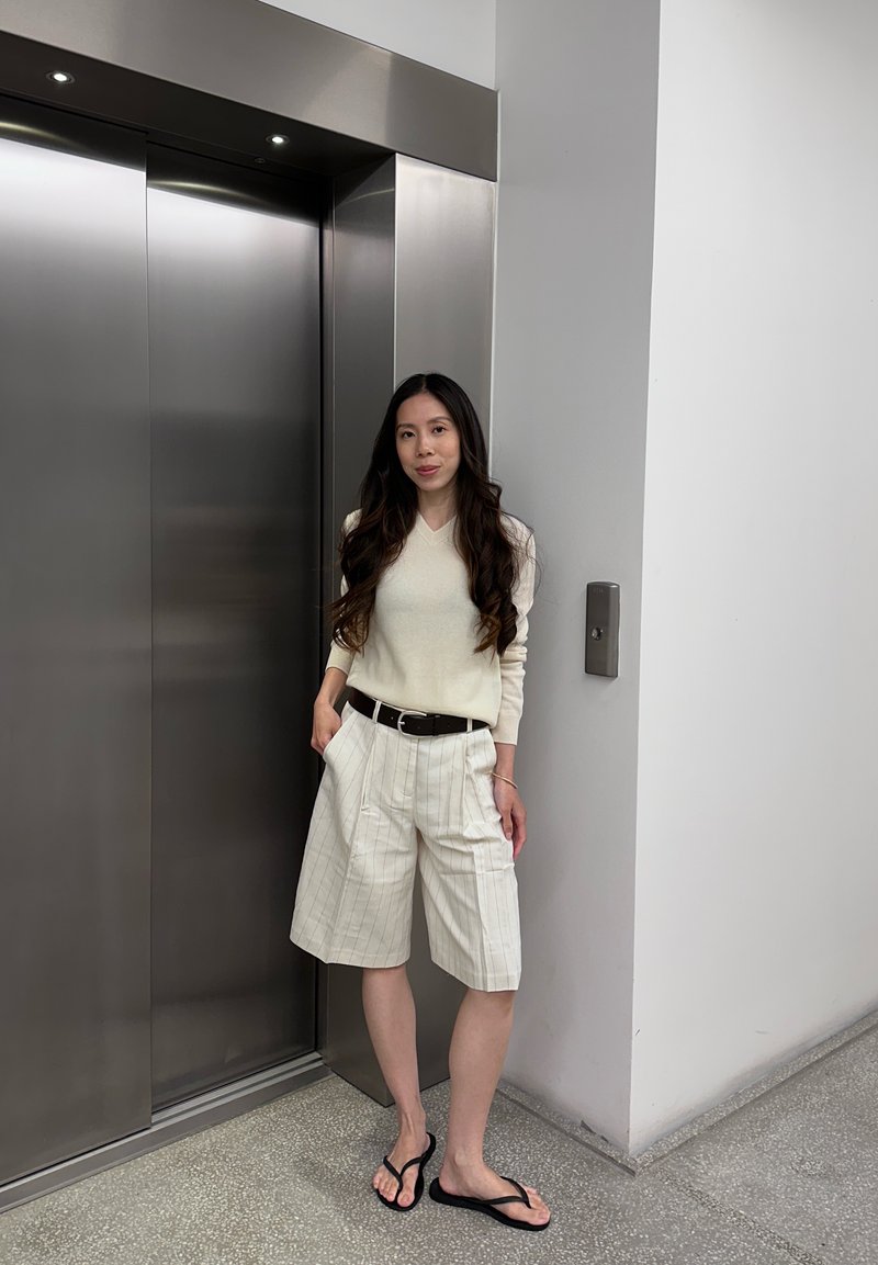 Femme portant un pull léger et un short rayé debout à côté de portes d'ascenseur en acier inoxydable fermées à l'intérieur.
