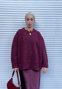 Vinrød oversized genser med teksturert finish, kombinert med en burgunder satengskjørt. Tilbehør med lagdelte gylne kjeder og en håndveske.