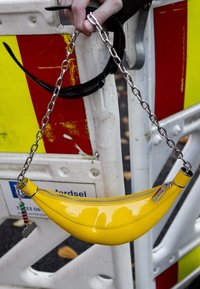 Gul lackläderhandväska i form av en banan, med en silverkedjeaxelrem och dragkedjestängning, samt en liten charm fästad.