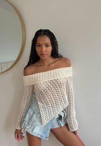 Maglioncino a spalle scoperte, lavorato a maglia in crema con un design a trama aperta. Abbinato a pantaloni cargo in denim azzurro chiaro con tasche laterali.