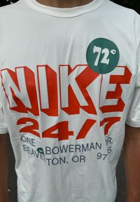 T-shirt en coton blanc avec un grand texte "NIKE" rouge, "24/7" en rouge, et un texte en gris avec une étiquette de prix circulaire verte affichant "72¢".