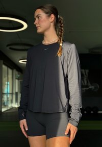 Juoda ilgomis rankovėmis sportinė palaidinė su apvalia iškirpte, derinamas su juodais šortais. Audinys atrodo lygus ir lengvas, turi subtilų blizgesį.