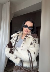 Jakna iz umetnega krzna v beli barvi s temno rjavimi madeži, z ovratnikom iz krzna, z zapiranjem na zadrgo in dolgimi rokavi; kombinirana z rjavo torbico.