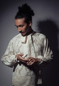 Blouse en dentelle écru avec un col montant, des manches longues et des poignets froncés ; présente un motif floral et une texture fluide et légère.