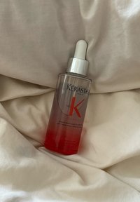 Kérastase Genesis anti-håravfall styrkende serum i en klar flaske med en hvit pipette, som hviler på beige stoff.