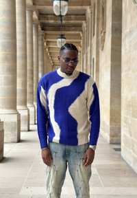 Pull en tricot avec des motifs ondulés bleus et beige, manches longues et poignets côtelés. Associé à un jean bleu clair avec des accents cousus.