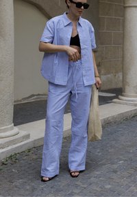 Modra in bela prugasta srajca z gumbi, v kombinaciji z ustreznimi hlačami na vezalko. Teksturna tkanina, širok kroj hlač in ravne sandale.