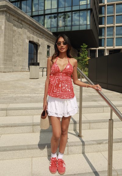 Top rojo de cuello halter con estampado floral blanco, combinado con una falda blanca con volantes y zapatillas rojas. Los accesorios incluyen gafas de sol y un bolso de mimbre.