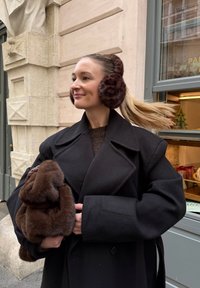 Cache-oreilles en fausse fourrure marron, manteau oversized noir et sac à main en fourrure marron. Texture lisse et couleurs chaudes pour un look hivernal confortable.