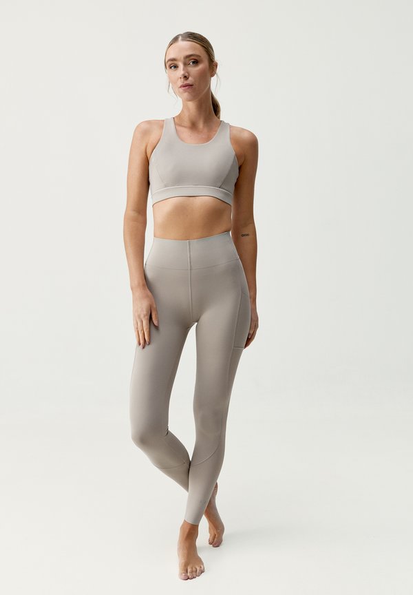Jasnoszary stanik sportowy i legginsy wysokiej talii wykonane z gładkiego, elastycznego materiału, charakteryzujące się bezszwowym designem i delikatnymi detalami przeszyć.
