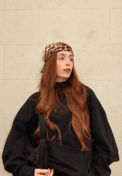 Pañuelo con estampado de leopardo marrón, sudadera negra de gran tamaño y bolso negro. Cabello largo y liso con textura suave. Fondo neutro.