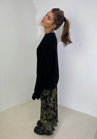 Black oversized sweater teamed with a long patterned skirt in dark green and gold, featuring frills at the hem. Black chunky boots.