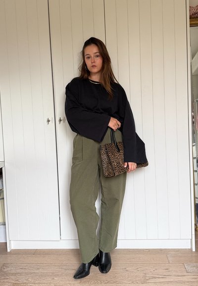 Top largo negro de manga larga oversize, pantalones de tiro alto en verde oliva de canalé y botas de tobillo negras puntiagudas. Sosteniendo un bolso de mano de estampado de leopardo.