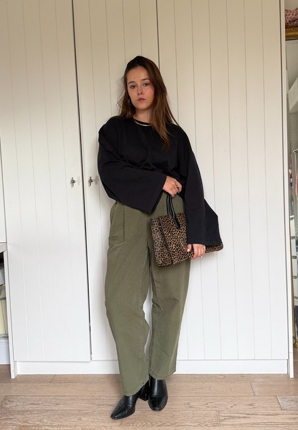 Oversized black long-sleeve top, olive green ribbed high-waisted trousers, and black pointed ankle boots. Carrying a leopard print handbag.