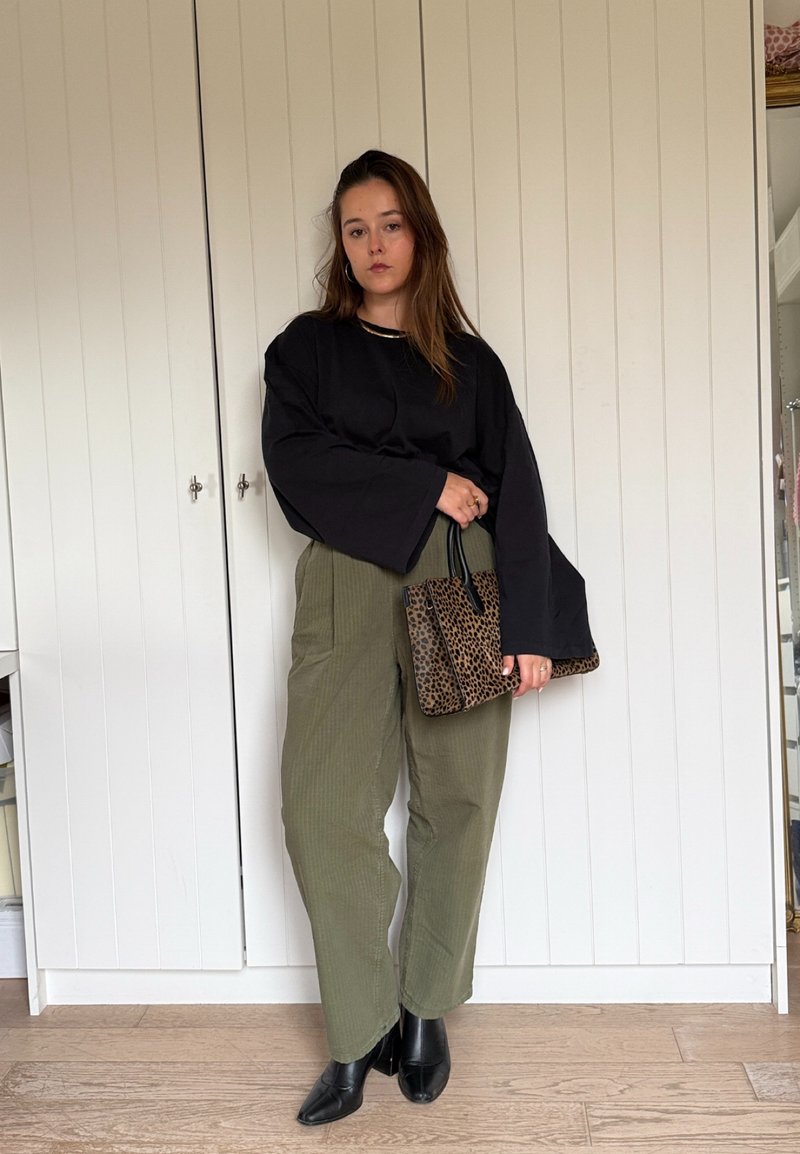 Black oversized long-sleeve top, olive green ribbed high-waisted pants, and black pointed ankle boots. Holding a leopard print handbag.