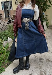 Denim dress with a fitted bodice, flared skirt, and silver-accented belt. Burgundy bomber jacket and black lace-up boots complete the look.