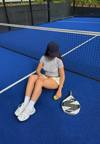 Padelschläger mit rundem Kopf und Löchern, neben einem grünen Tennisball auf einem leuchtend blauen Tennisplatz platziert.