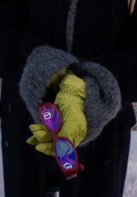 Άτομο που φοράει γκρι μάλλινα γάντια πάνω από πράσινα γάντια κρατά γυαλιά ηλίου με κόκκινο σκελετό και μπλε φακούς έναντι μαύρο υ παλτού.