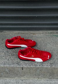 Κόκκινα σουέτ αθλητικά παπούτσια με λευκή λωρίδα της Puma, χρυσό λογότυπο και μαύρη καουτσούκ σόλα. Διαθέτουν στρογγυλή μύτη και σχέδιο με κορδόνια.