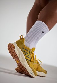 Gula sportskor med grå accenter och textilier, med gummisula och framträdande snörning. Matchas med vita ribbade strumpor.