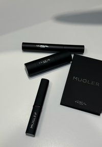 Trzy czarne tuby kosmetyczne i czarna książeczka z połyskującym, srebrnym napisem. Opakowanie ma elegancki, minimalistyczny design.