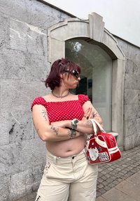 Top cropped vermelho com bolinhas brancas e mangas bufantes, calças cargo bege, joias prateadas e uma bolsa da Hello Kitty vermelha com detalhes brancos.