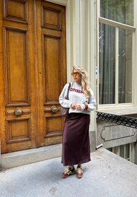 Szara bluza z napisem "Kopenhaga", brązowa satynowa długa spódnica, brązowe i złote sneakersy oraz brązowa torba na tle drewnianych drzwi.