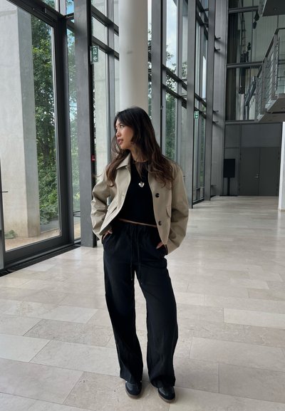 Chaqueta corta beige, top negro, pantalones negros holgados y zapatos negros. Texturas suaves, diseño clásico con botones y cintura ajustable.