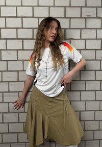 Weisses Trikot mit roten und orangenen Akzenten, kombiniert mit einem khakifarbigen Rock mit ausgestelltem Design, Taschen und einem Reißverschlussdetail.