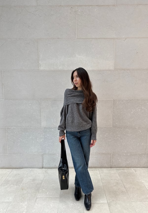 Pilkas off-shoulder megztinis su šonkaulinėmis rankovėmis, derinamas su mėlynomis plačiomis kelnėmis. Juoda rankinė ir juodi auliniai batai užbaigia įvaizdį.